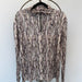A long-sleeve quarter-zip pullover top with an abstract bark-like camouflage pattern in brown, beige, and gray, hanging on a black hanger from a decorative metal coat rack.